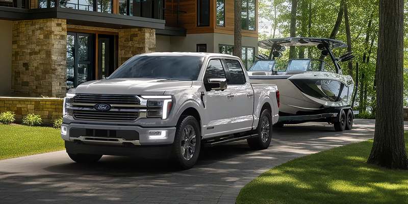 White Ford F-150 pickup truck towing a boat, parked in front of a modern lakeside home.