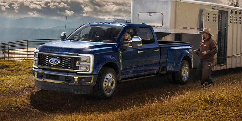 Blue Ford Super Duty pickup truck towing a horse trailer on a rural ranch with a driver and rancher standing nearby.