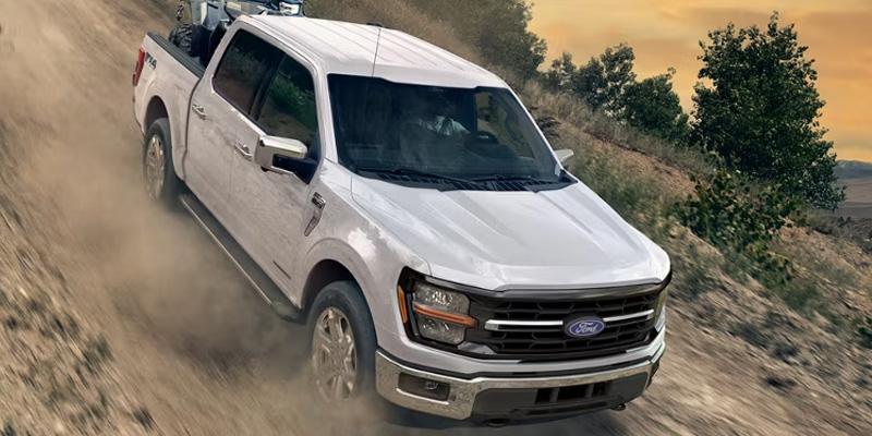 White Ford pickup truck driving through a dusty off-road trail.