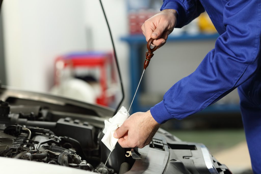 Mechanic checking engine oil level with a dipstick under the hood.