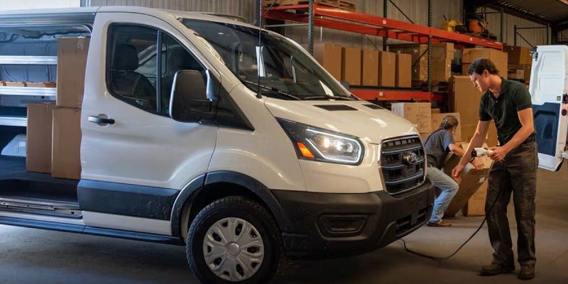 White Ford Transit van being loaded with equipment in a warehouse.